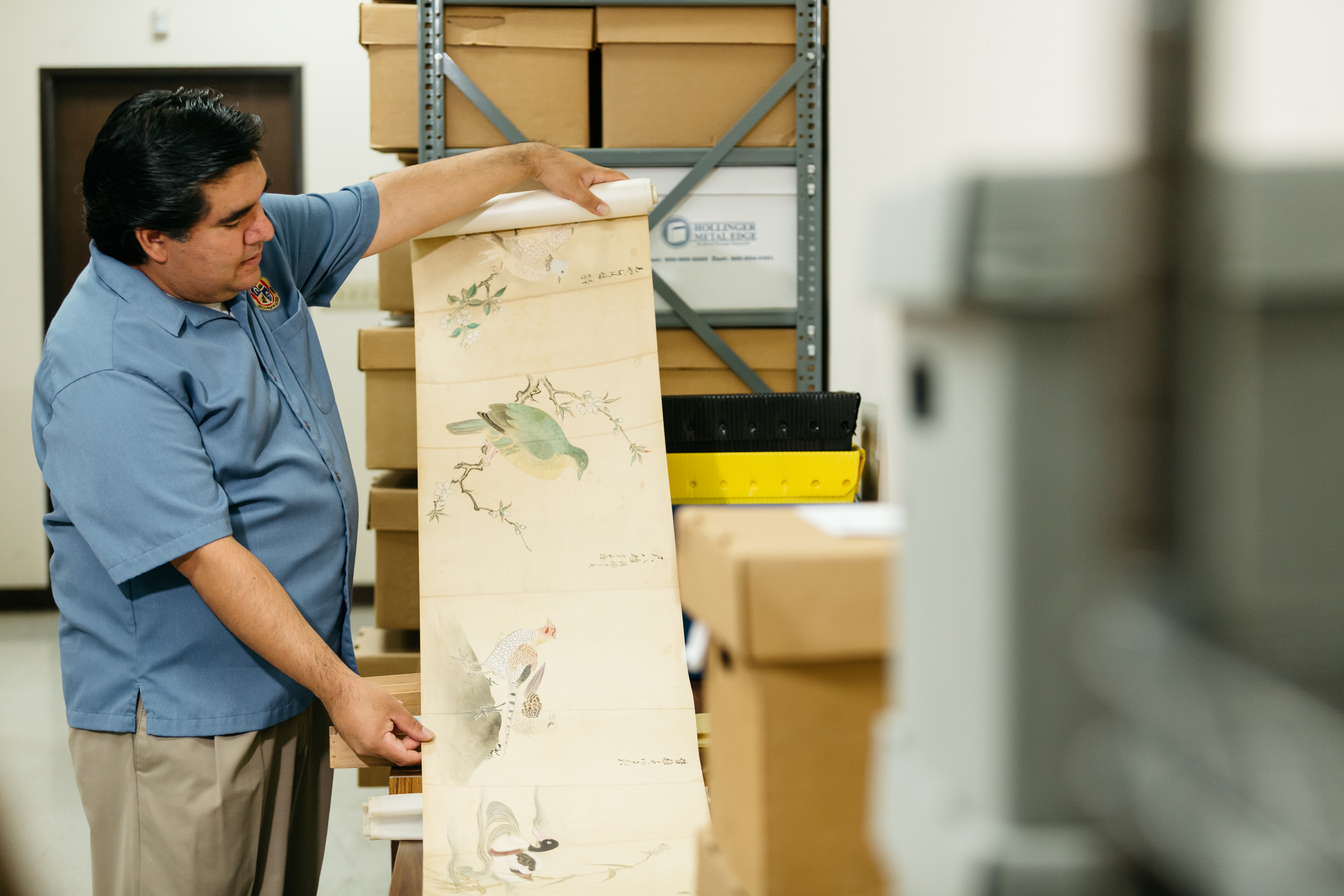 A narrow aisle between large, high-density storage shelves in a modern archival facility. The shelves are labeled and equipped with handles, designed for efficient storage and retrieval of documents or files.